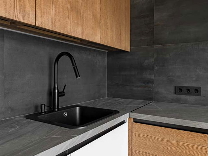 kitchen sink with black faucet and dark grey countertop and backsplash